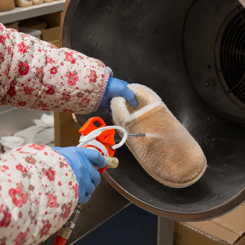 Worker using compressed air to remove loose fibers from plush slippers before packing